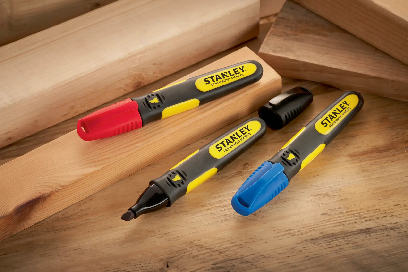 STANLEY SKU 0-47-315 rotuladores permanentes con tapas roja, azul y negra sobre tablas de madera, vista en ángulo.
