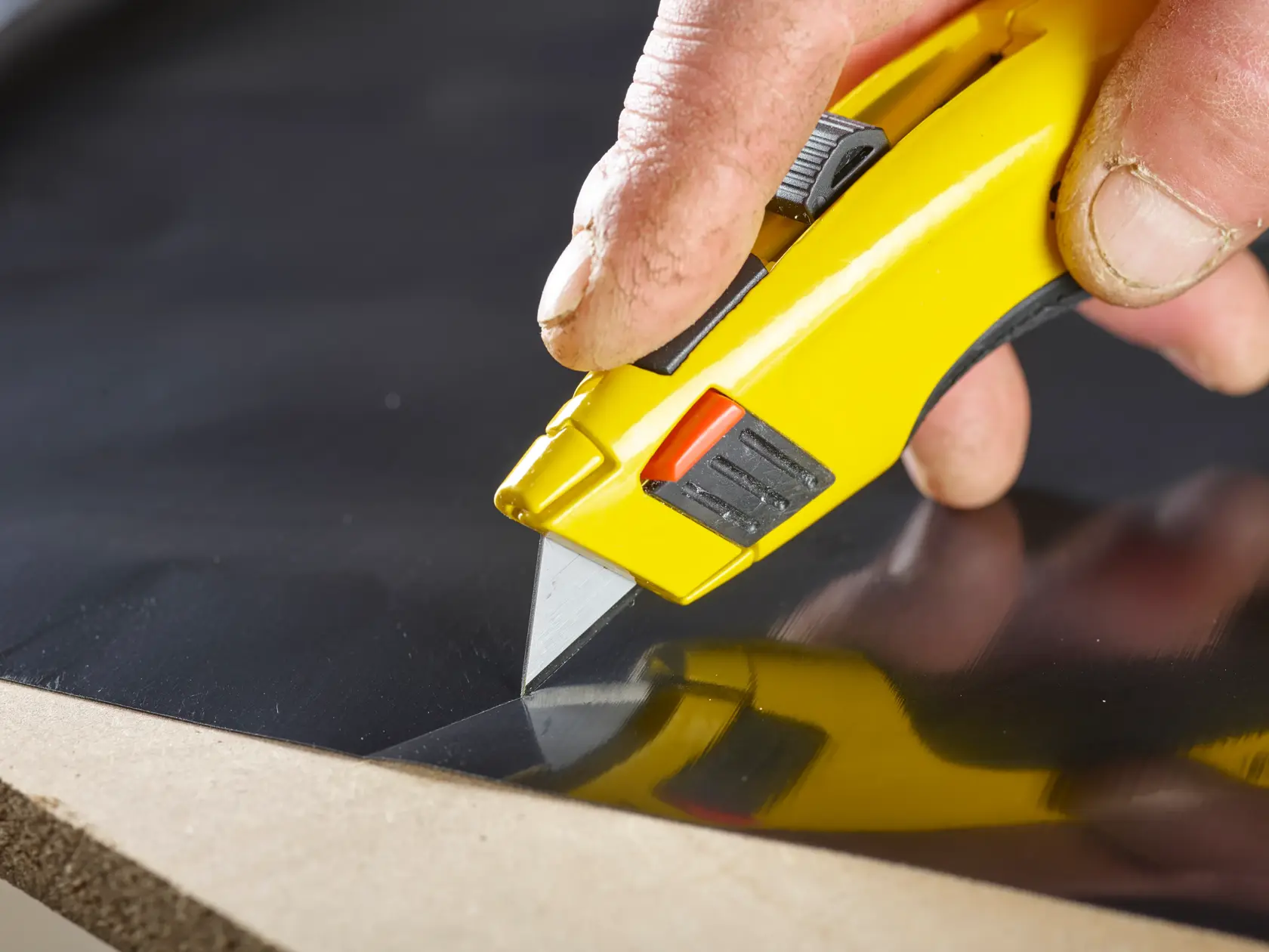 STANLEY 1-11-921 cuchillo utilitario cortando material negro, fotografía en primer plano del mango amarillo y la hoja en uso.
