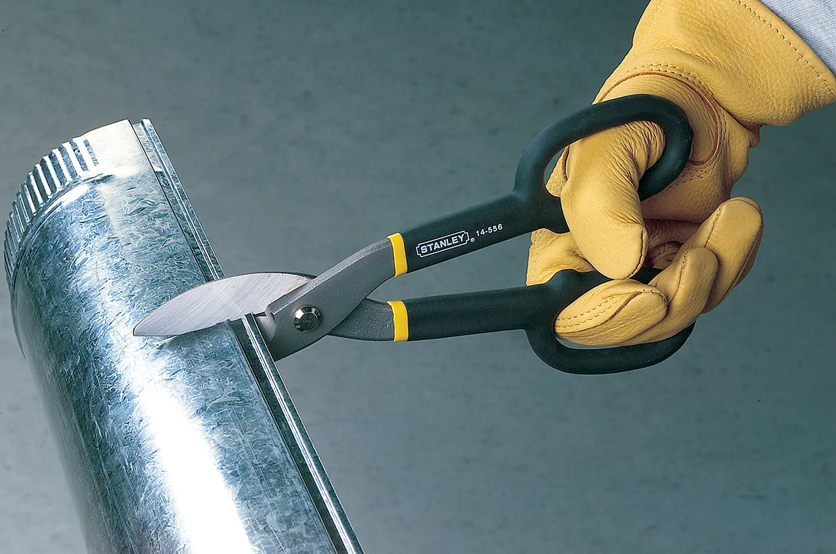 Stanley 14-556 tijeras para cortar metal en uso, mangos negros y amarillos, cortando tubo galvanizado.
