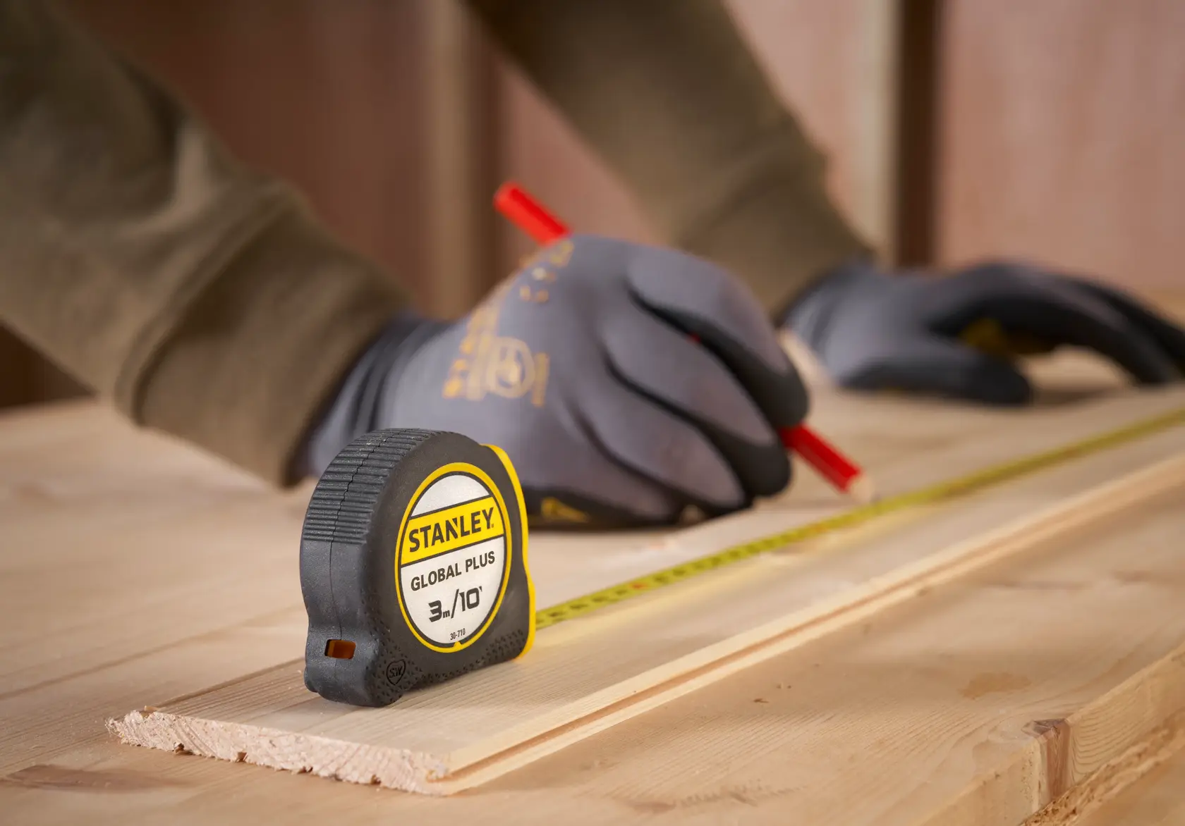 Cinta métrica STANLEY 30-710 sobre madera, persona con guantes marcando una tabla con lápiz.