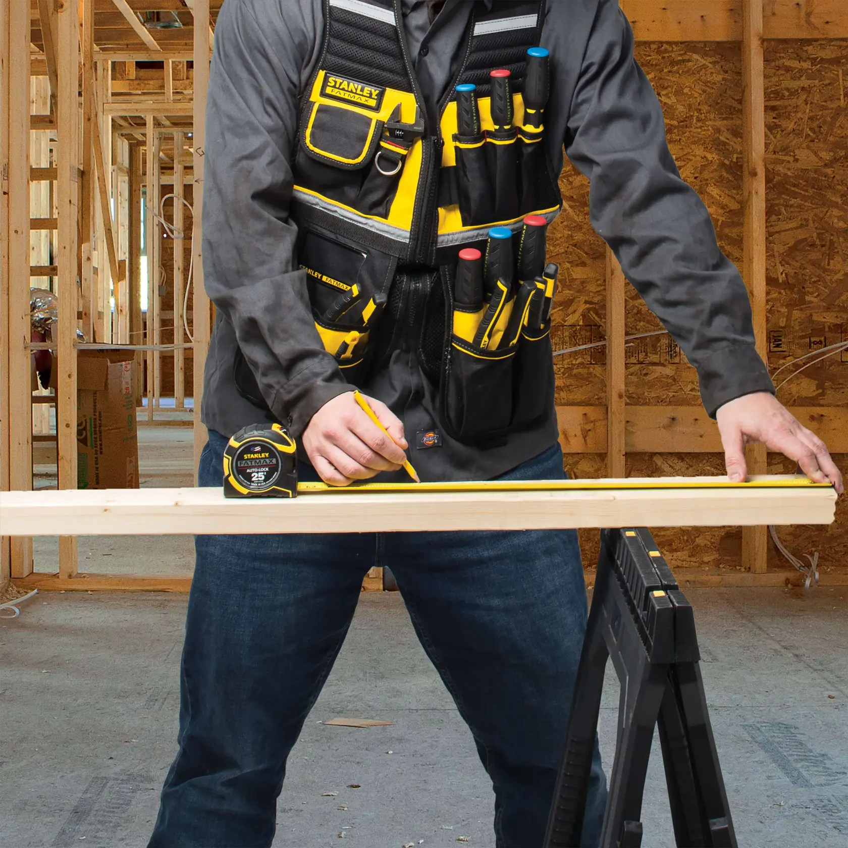 Fotografía del chaleco porta herramientas STANLEY FMST530201 con varios bolsillos, usado por persona marcando madera en taller.