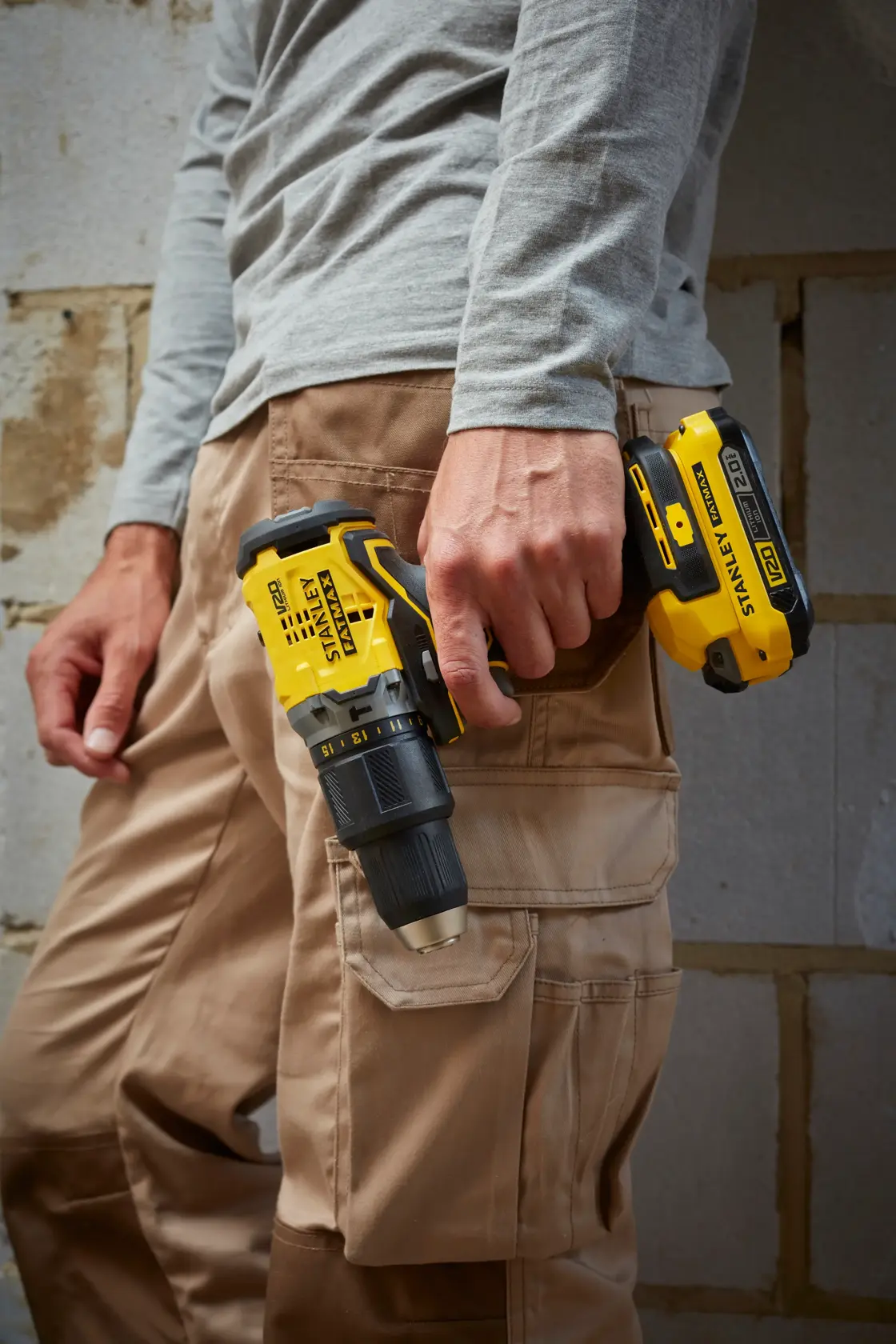 Fotografía de persona sosteniendo taladro inalámbrico STANLEY SBD715C2K-B2 en la mano derecha, de pie junto a una pared.