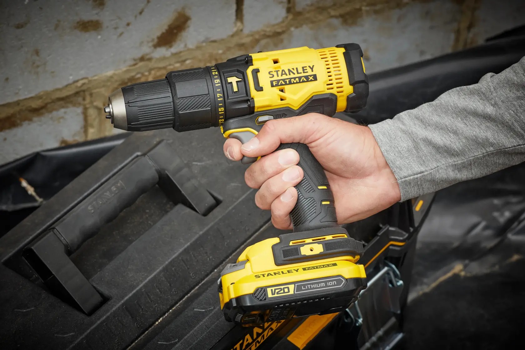 Taladro inalámbrico STANLEY SCD711C2K-BR en mano, diseño amarillo y negro, junto a caja de herramientas.