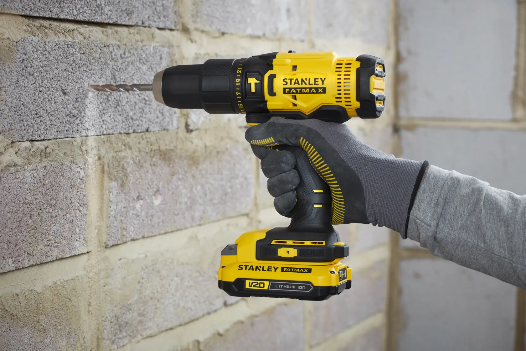 Stanley SCD711C2K-BR taladro inalámbrico amarillo y negro, vista lateral, perforando pared de ladrillo.