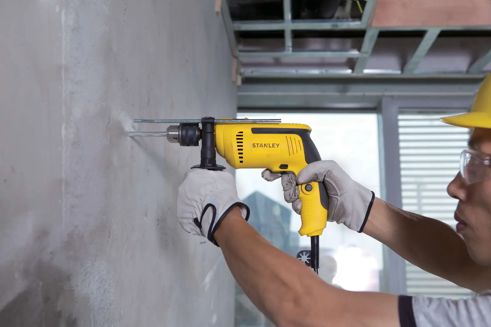 Taladro con cable STANLEY SDH700K en uso sobre pared de concreto, vista lateral, diseño amarillo y negro, categoría herramienta eléctrica.