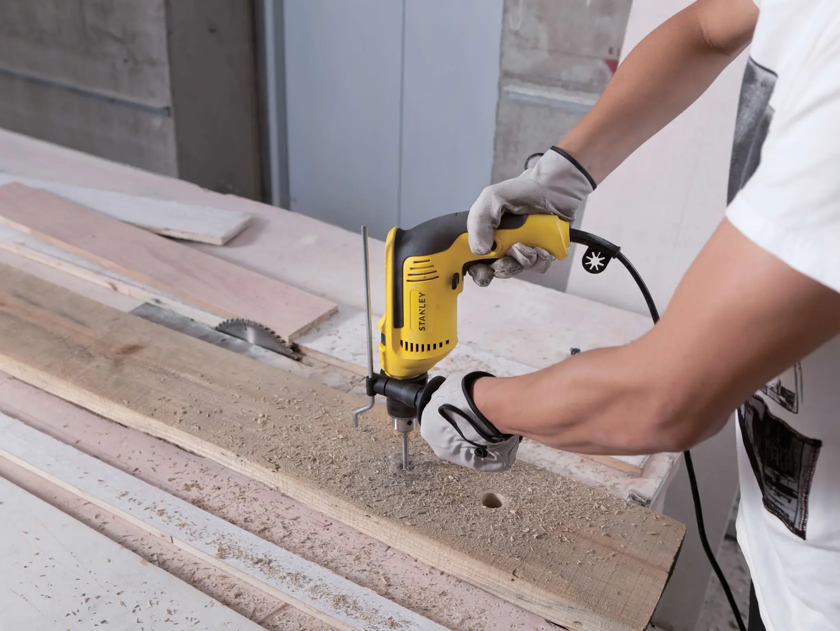 STANLEY SDH700K taladro usado en madera, primer plano de manos enguantadas sosteniendo herramienta eléctrica amarilla.
