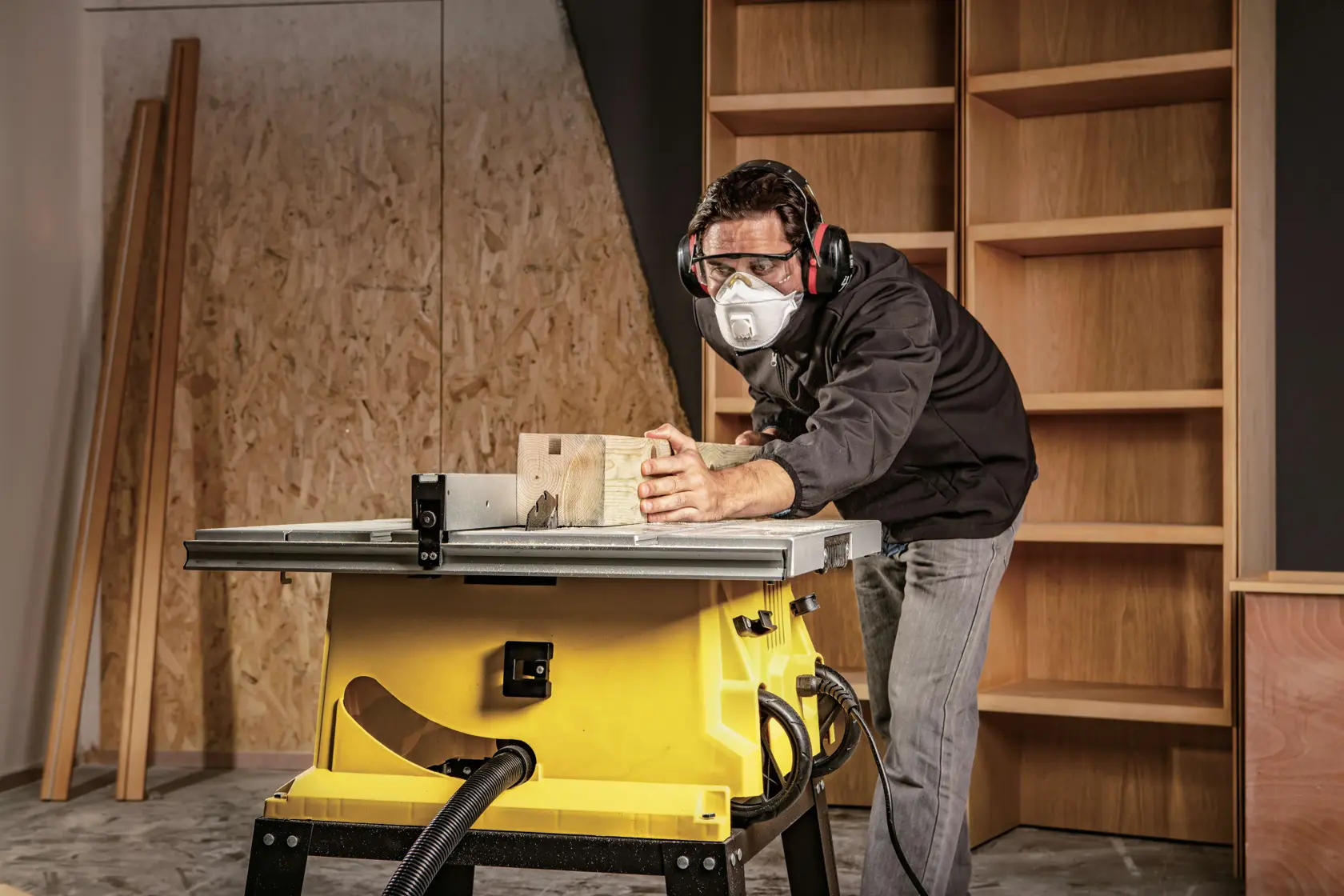 Sierra de mesa STANLEY SST1801-B3 en taller, vista lateral, cortando madera con operador usando protección auditiva.