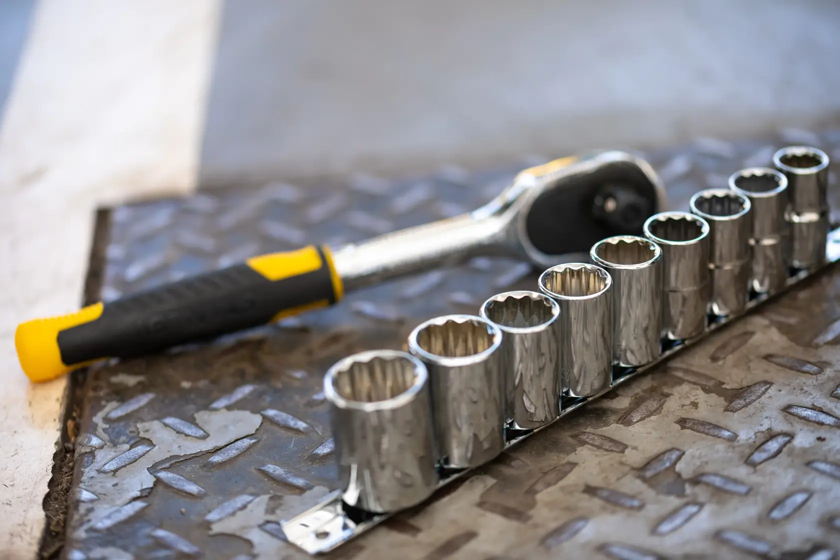 Llave de carraca STANLEY STMT82671-0 con mango negro y amarillo y juego de dados sobre superficie metálica, vista lateral.