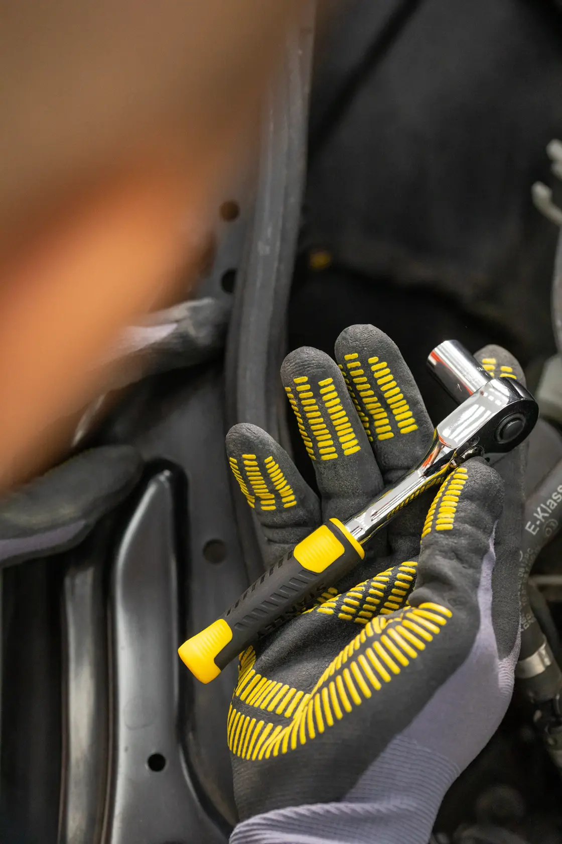 Fotografía de la llave de carraca STANLEY STMT82828-LA con mango negro y amarillo, sostenida por una mano enguantada en uso.