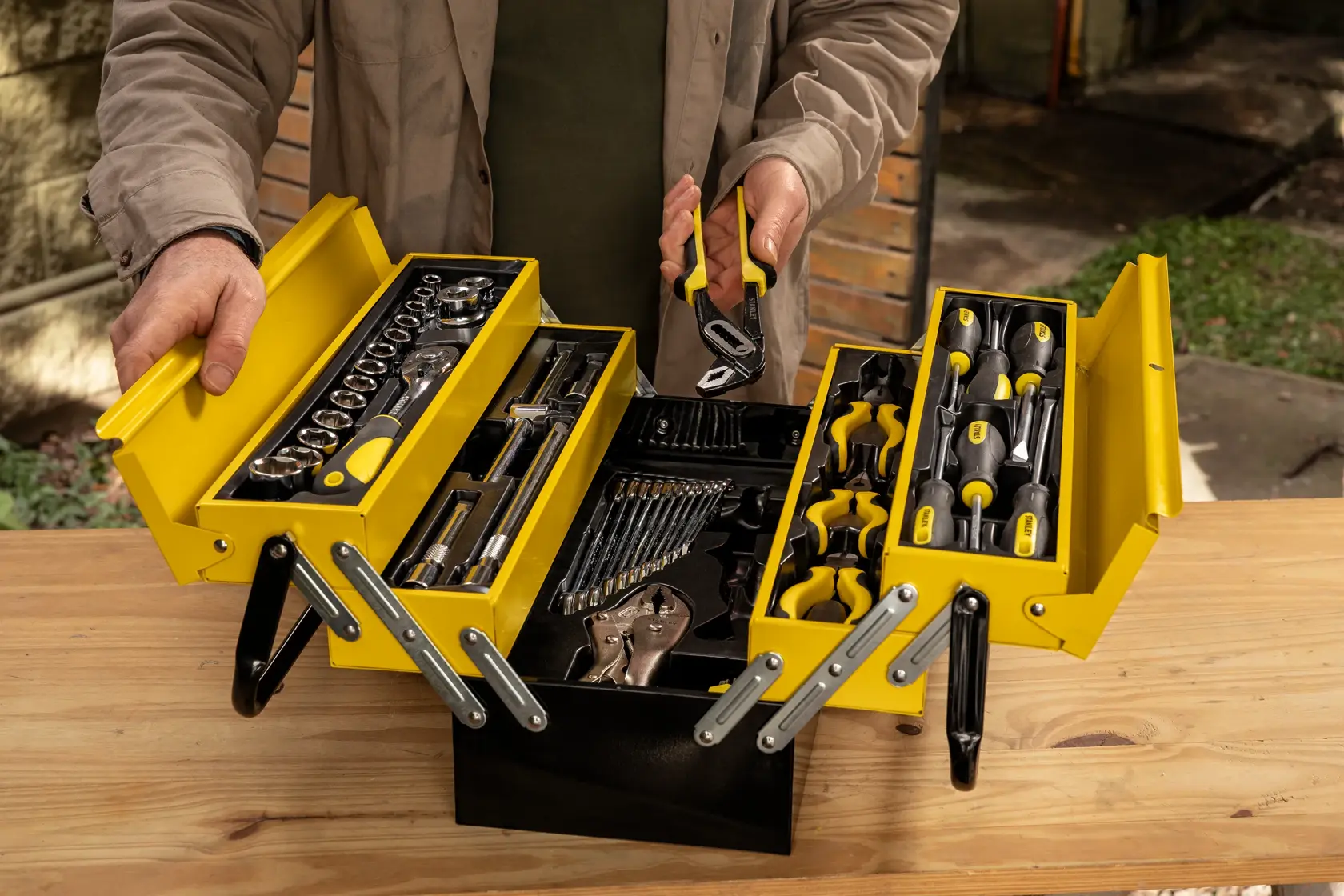 Caja de herramientas metálica amarilla STANLEY STMT98087-LA con herramientas manuales y dados, vista superior, sobre mesa de madera.